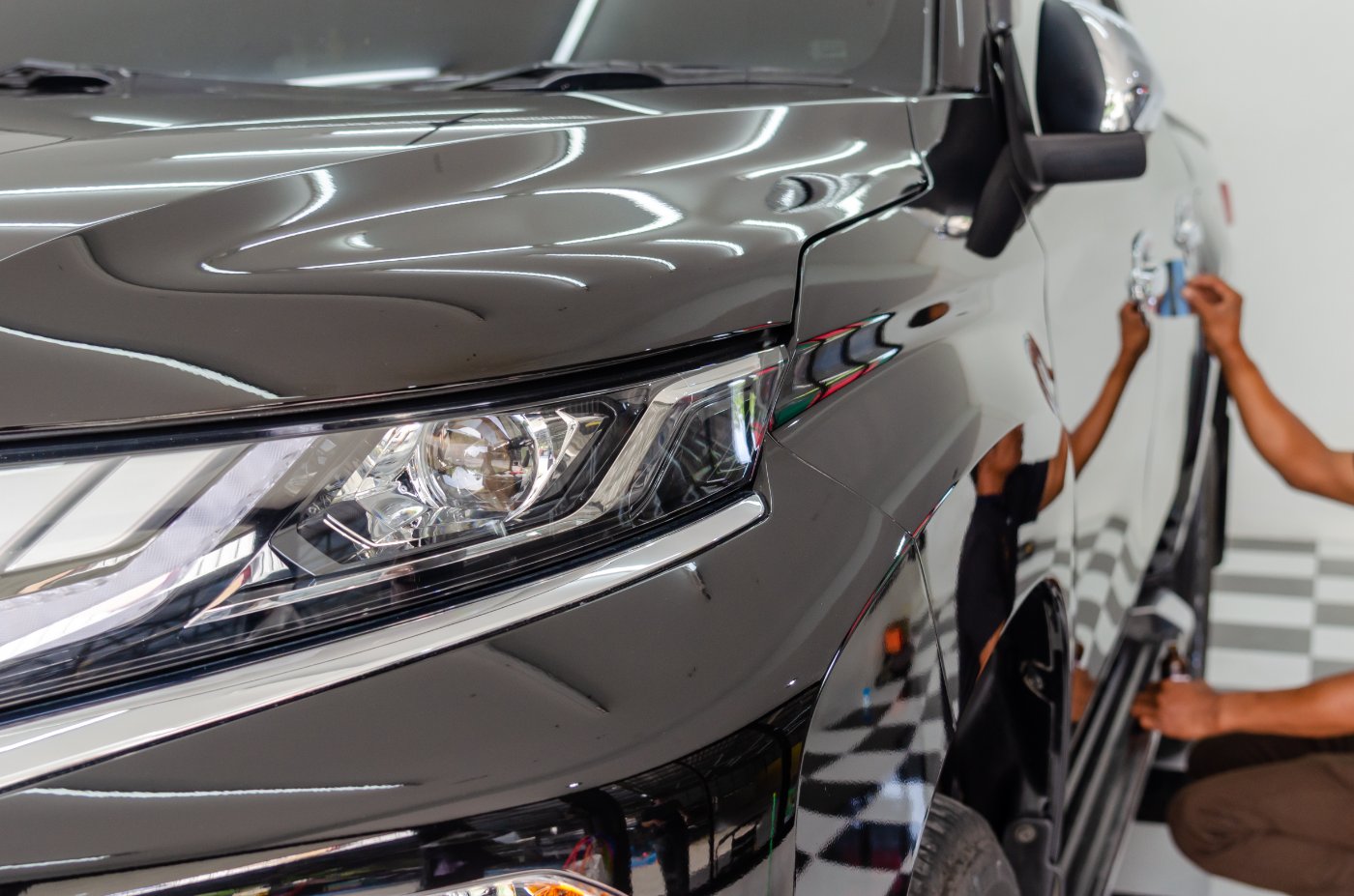 Professional car detailing worker applying protective coating to vehicle hood