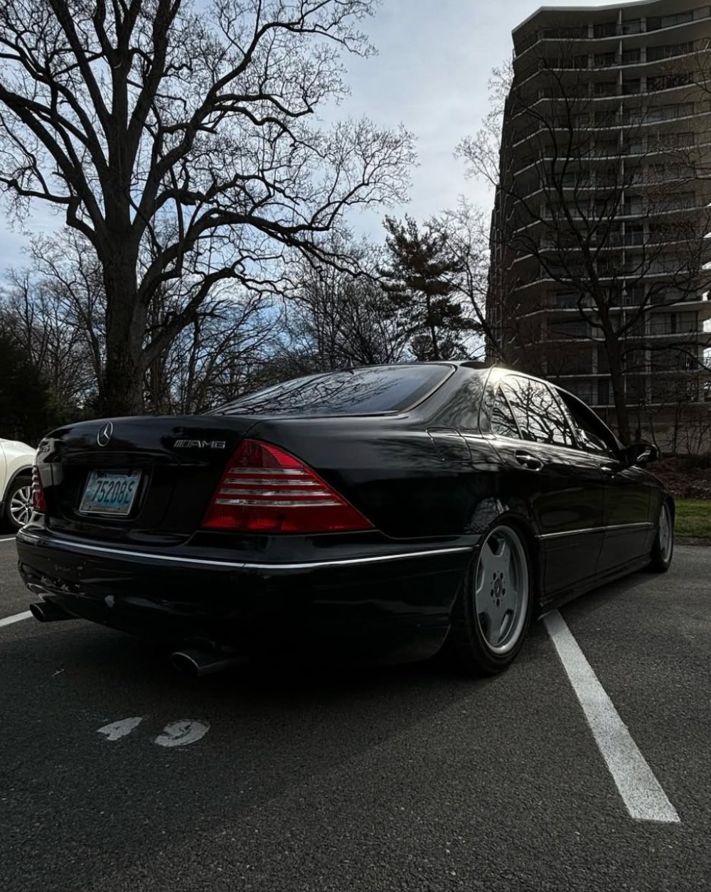 Black Mercedes-Benz AMG sedan parked in lot with bare trees and apartment building