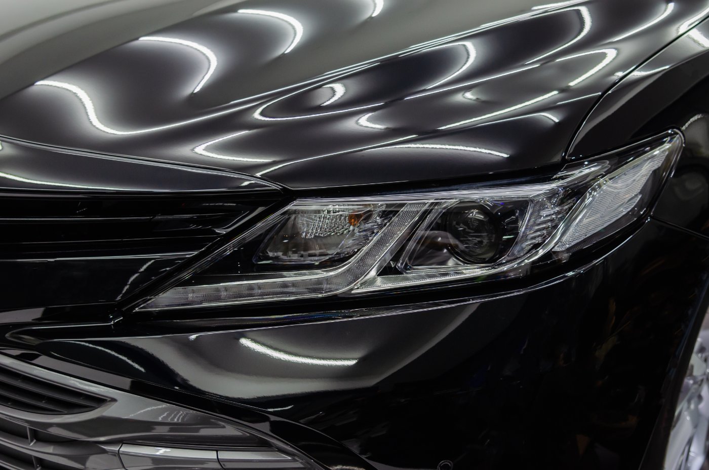 Close-up of sleek black car headlight and hood with chrome trim in showroom