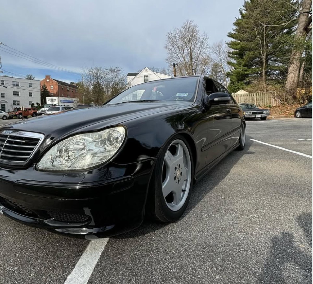Black Mercedes-Benz sedan parked in lot with trees and buildings in background