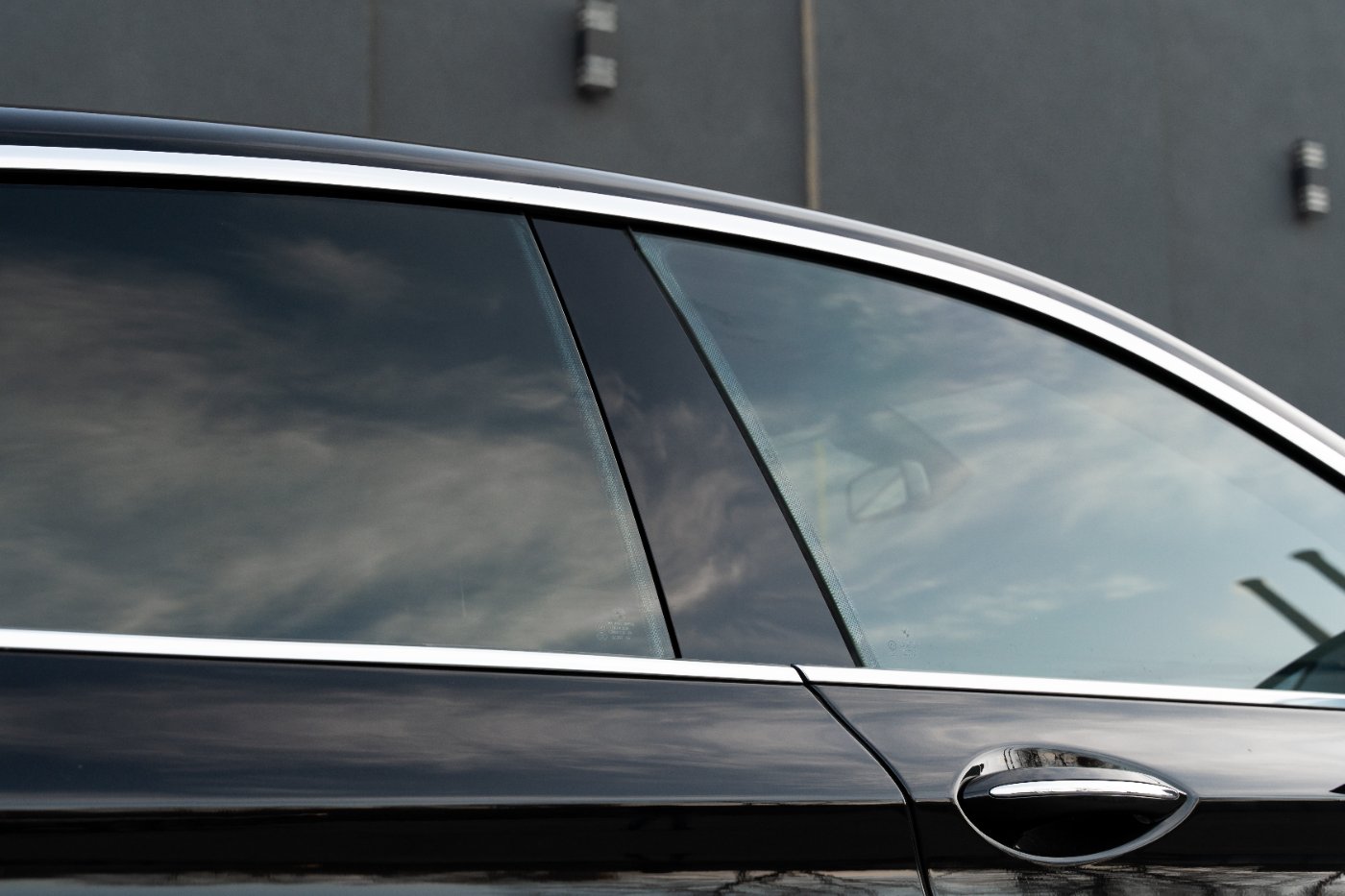 Side profile of dark sedan showing tinted windows and chrome door handle against gray building